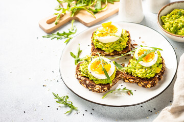 Avocado sandwich. Whole grain bread with avocado and boiled eggs with arugula. Top view on white background.