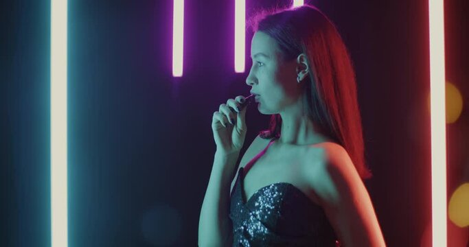 Side view of beautiful woman vaping exhaling smoke and smiling in dark space with neon illumination. Night life and millennial concept.