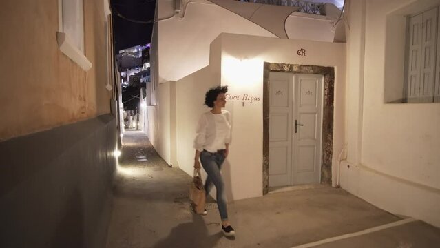 Woman walks on narrow Cori Rigas street in Fira, Santorini at night