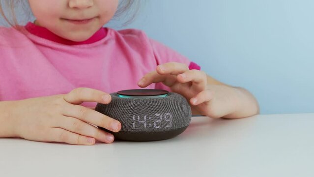 Little Child Using Smart Speaker At Home While Doing Homework. Home Robot. Education Programme For Child. Kid Girl Talking To Smart Speaker And Give It Orders And Commands. Smart Home Concept
