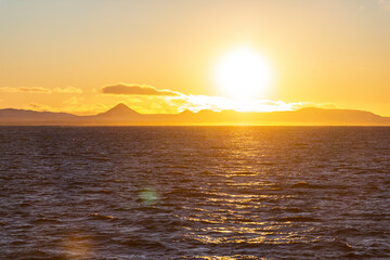 imagen de la puesta de sol sobre el mar y unas montañas en el horizonte 