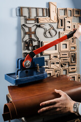 Craftsman is using leather punching press for creating forms from genuine leather. Process of creating genuine leather products in factory.