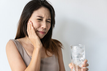 Young Asian woman feeling teeth pain. Closeup of sad girl suffering from sensitive teeth after drinking cold water. Dental health and care, teeth problem concept. Copy space