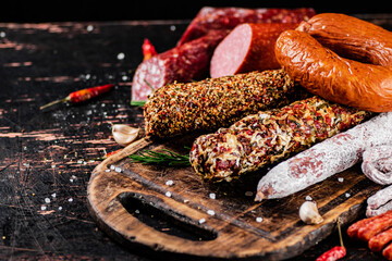 Different types of salami sausage on a cutting board with rosemary. 