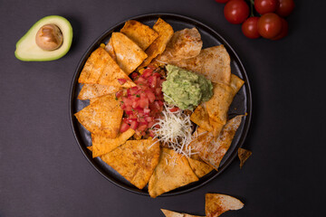 dry bread, tomatoes, cheese, sauces, avocado in a black plate on a dark background