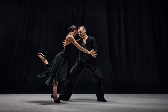 Man and woman, professional tango dancers performing in black stage costumes over black background. Choreography. Concept of hobby, lifestyle, action, motion, art, dance aesthetics