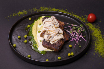 fried pork with mushroom and cream sauce, microgreens in a black plate on a dark background