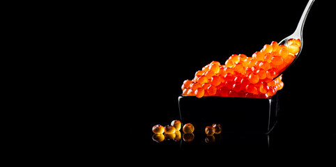 Red Caviar in a spoon. Salmon caviar in bowl isolated on black background. Close-up salmon caviar....