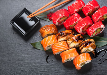 Sushi with chopsticks. Sushi roll japanese food in restaurant. California Sushi roll set with salmon, vegetables, flying fish roe and caviar closeup. Japan restaurant menu. Top view