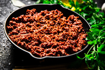 Bolognese sauce in a frying pan with pasta dry and parsley. 