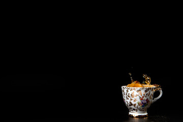 Splash in vintage cup of black tea isolated on black background with delicious cookies, copy space...