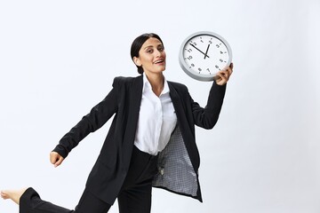 Business woman holding a wall clock in a black business suit and glasses showing signals gestures...