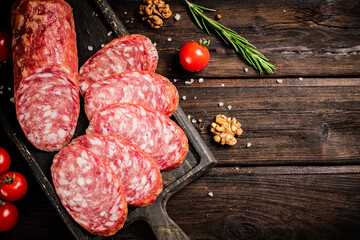 Pieces of salami sausage on a cutting board with cherry tomatoes and rosemary.