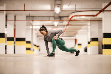 Obraz premium A fit sportswoman is stretching her leg in underground garage.