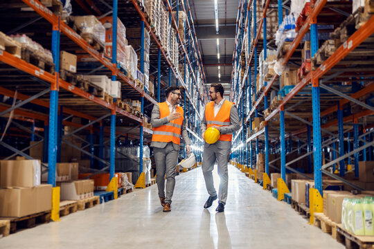 Two associates walks in warehouse full of goods and talks about commodity reserves.