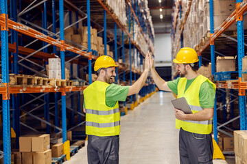 Two warehouse clerks giving each other high five for teamwork in import and export firm.