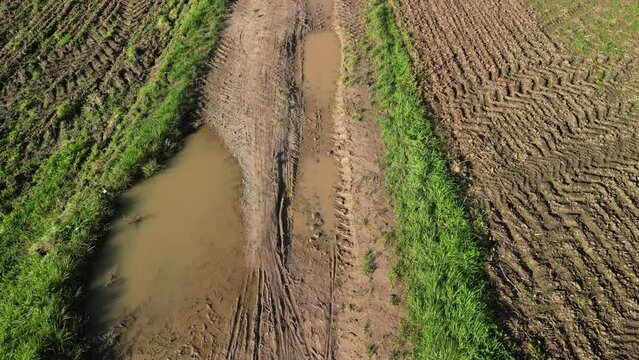 Drone flight over of a dirt road with puddles, water and mud next to agricultural fields in autumn after rain, Germany