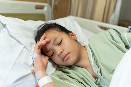 Asian woman patient with medical drip have headache with migraine headaches hospital ward, teenager sick in hospital with saline intravenous, Selective focus, healthcare and health insurance concept.