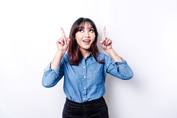 Obraz na płótnie Canvas Excited Asian woman wearing blue shirt pointing at the copy space on top of her, isolated by white background