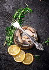 Pieces of salted herring in a jar with rosemary and lemon. 