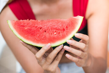 Asian beauty woman holding big red sliced watermelon at face sea only eye. Girl bite sliced...