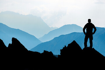One Man reaching summit after climbing and hiking enjoying freedom and looking towards mountains silhouettes panorama during sunrise.