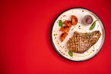 Fototapeta na wymiar grilled pork steak on a white plate on a red background dish