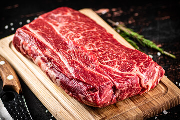 Raw beef on a wooden cutting board with rosemary.