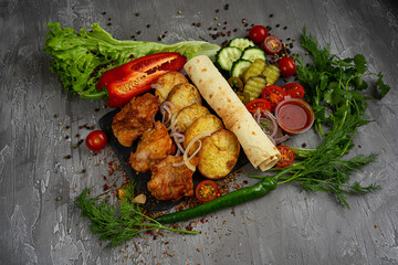 Turkey meat on the grill with fried potatoes, cucumbers, cherry tomatoes and ketchup on a gray background, pita bread, greens, dill