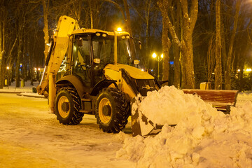cleaning snow in the park in winter with a tractor in the evening