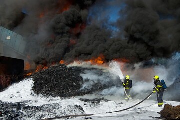 Firefighters use foam to extinguish a massive fire of large amounts of plastic waste