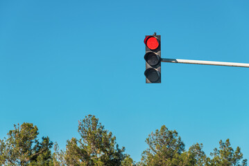 Modern traffic light with red light in front of cloudless sunny blue sky