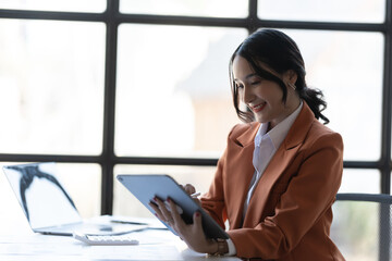 Young asian woman, company worker in red suit, smiling and holding digital tablet while working.