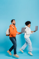 full length of stylish multiethnic students with backpacks and laptops levitating on blue background.