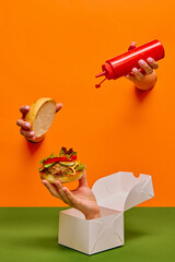 Food pop art photography. Female hand sticking out orange paper with ketchup over burger on hand...