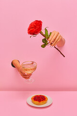 Food pop art photography. Female hand sticking out pink paper with champagne and rose flower over delicious berry tart. Concept of taste, creativity, art. Complementary colors. Copy space for ad, text