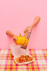 Food pop art photography. Female hand sticking out pink paper and grating yellow pepper on spaghetti with meatballs. Concept of taste, creativity, art. Complementary colors. Copy space for ad, text