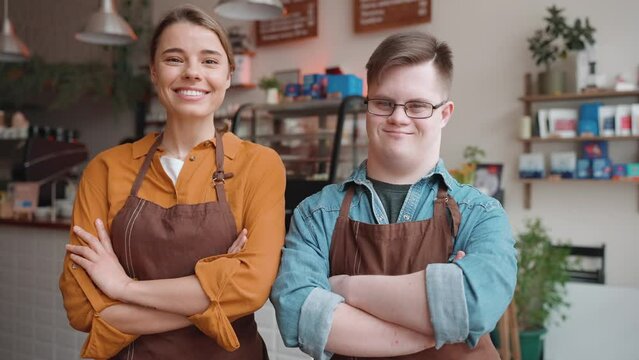 Happy male waiter with Down syndrome standing with a girl colleague and looking at the camera in the cafe