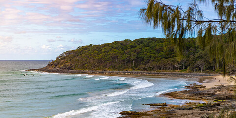 panorama of noosa national park at sunset; group of surfers surfing in the paradise bay in queensland, australia