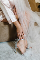 Bride putting on her stylish silver shoes or sandals. Wedding morning preparation in home. Bottom...