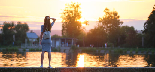 Young woman in casual outfit relaxing on lake side on warm evening. Summer vacations and travelling concept