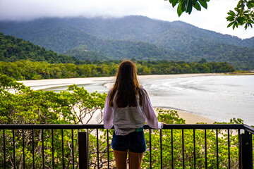 woman standing on balcony admiring panorama of daintree rainforest and beach at cape tribulation in...