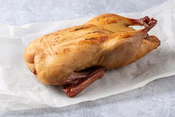Smoked duck whole on baking paper on gray background.