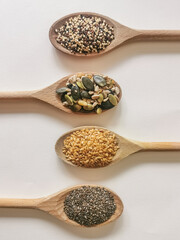 View of four wooden spoons on white background with various types of seeds: sesame, chia, sunflower and pumpkin seeds. Theme for healthy, vegetarian or modern cuisine commercial