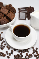 Coffee ceramic cup with milk jug, cake, chocolate and coffee beans on a white background