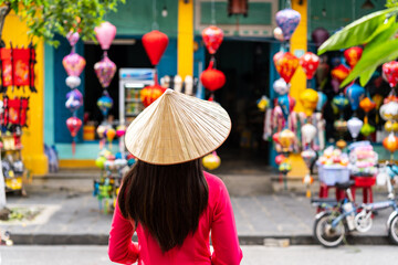 Young female tourist in Vietnamese traditional dress looking at a souvenir shop in Hoi An Ancient town