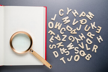 Scattered English alphabets with magnifying glass on the empty page of an opened book, keyword...