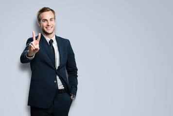 Excited businessman in black confident suit showing two fingers or victory sign gesture, against...