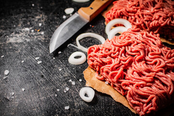 Fresh minced meat on paper on a table with a knife and onion rings.