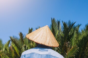 A fisherman wears vietnamese hot (Asian conical hat) with coconut palm tree and blue bright sky background, Hoi an bamboo basket boat local tour
